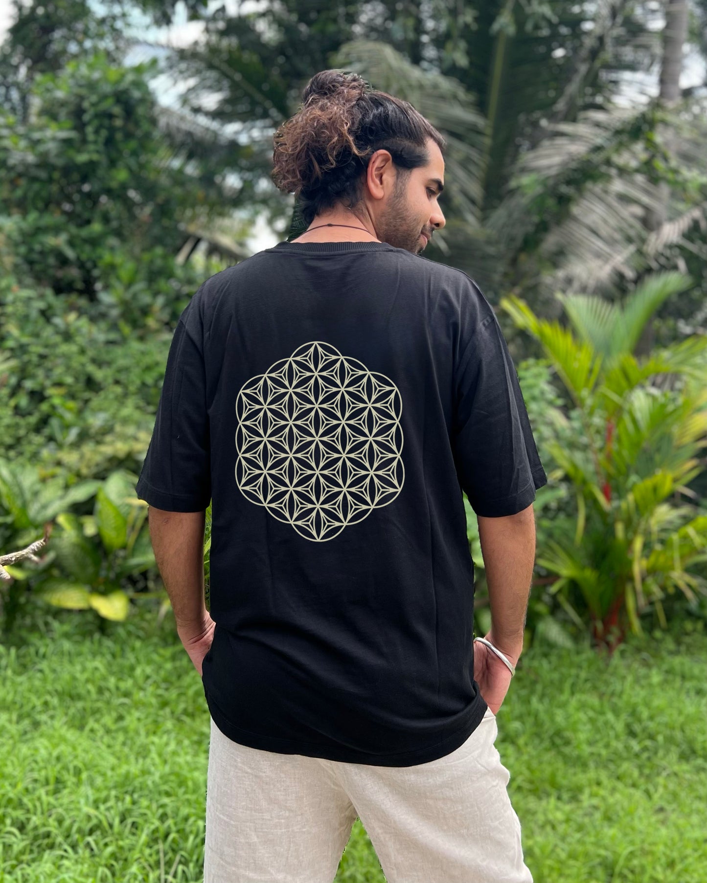 Person wearing a black t-shirt with a geometric design on the back, standing in a lush green outdoor setting.