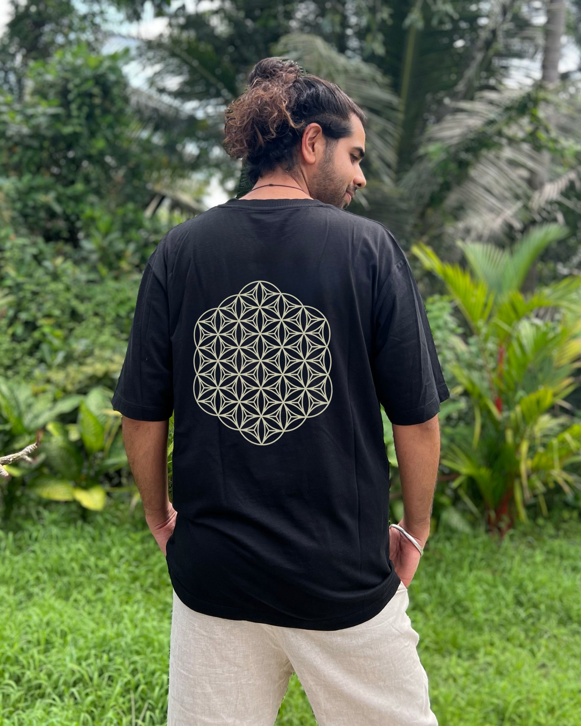Person wearing a black t-shirt with a geometric design on the back, standing in a lush green outdoor setting.