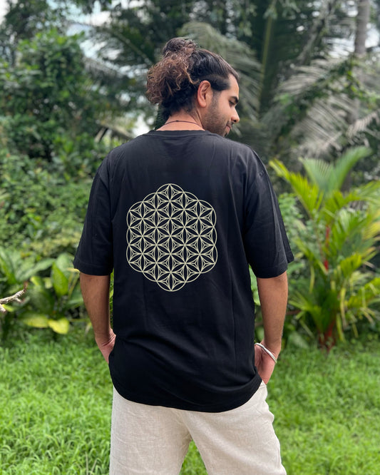 Person wearing a black t-shirt with a geometric design on the back, standing in a lush green outdoor setting.