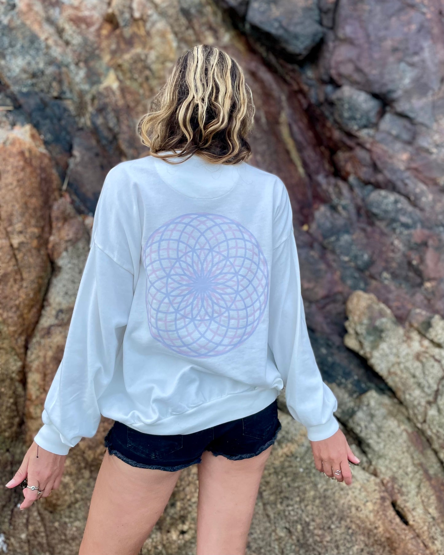 Person wearing a white sweatshirt with a geometric design, standing against a rocky background.
