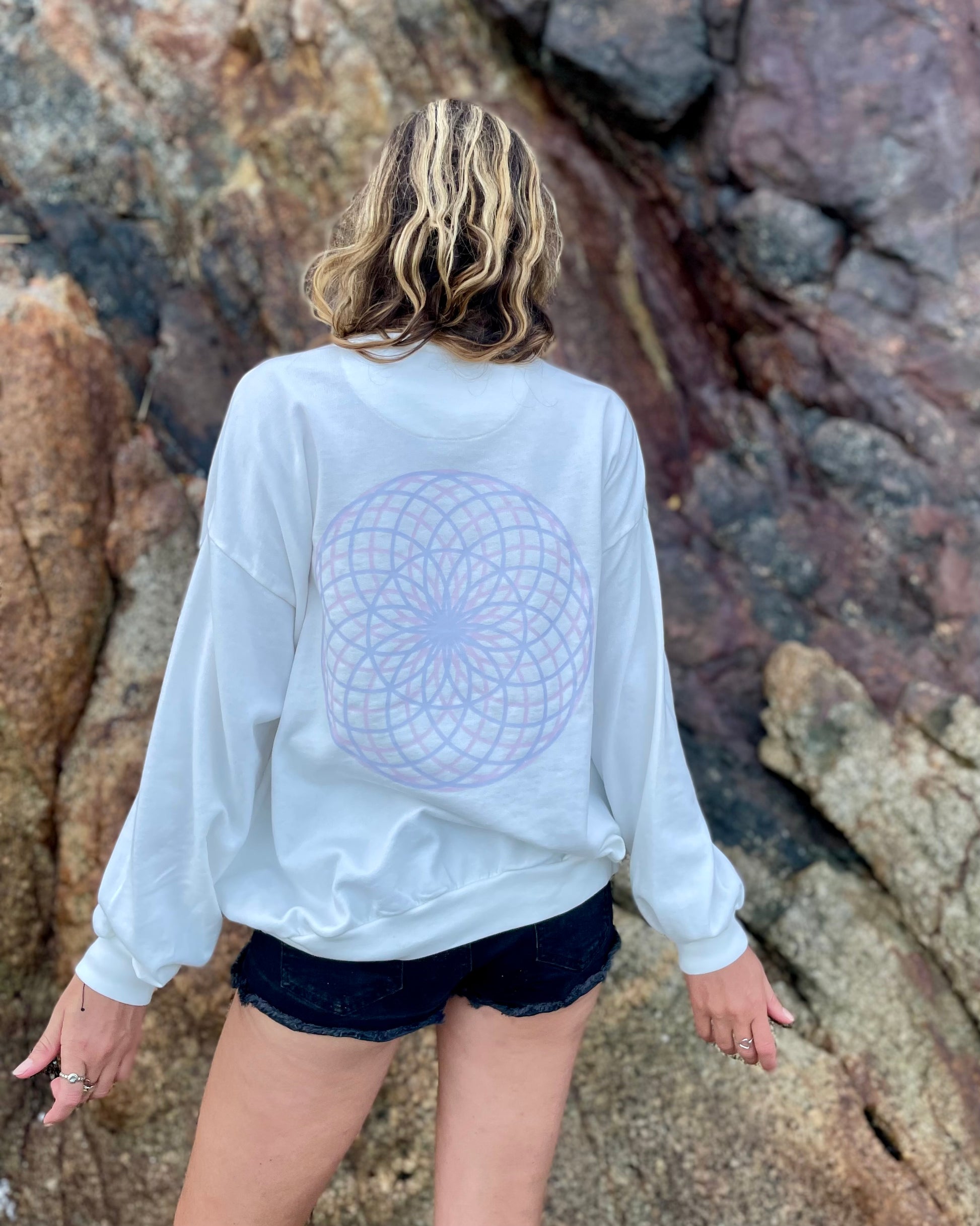 Person wearing a white sweatshirt with a geometric design, standing against a rocky background.