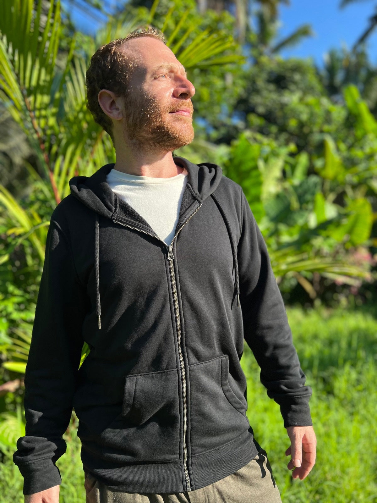 Man wearing a black hoodie standing in a lush green outdoor setting