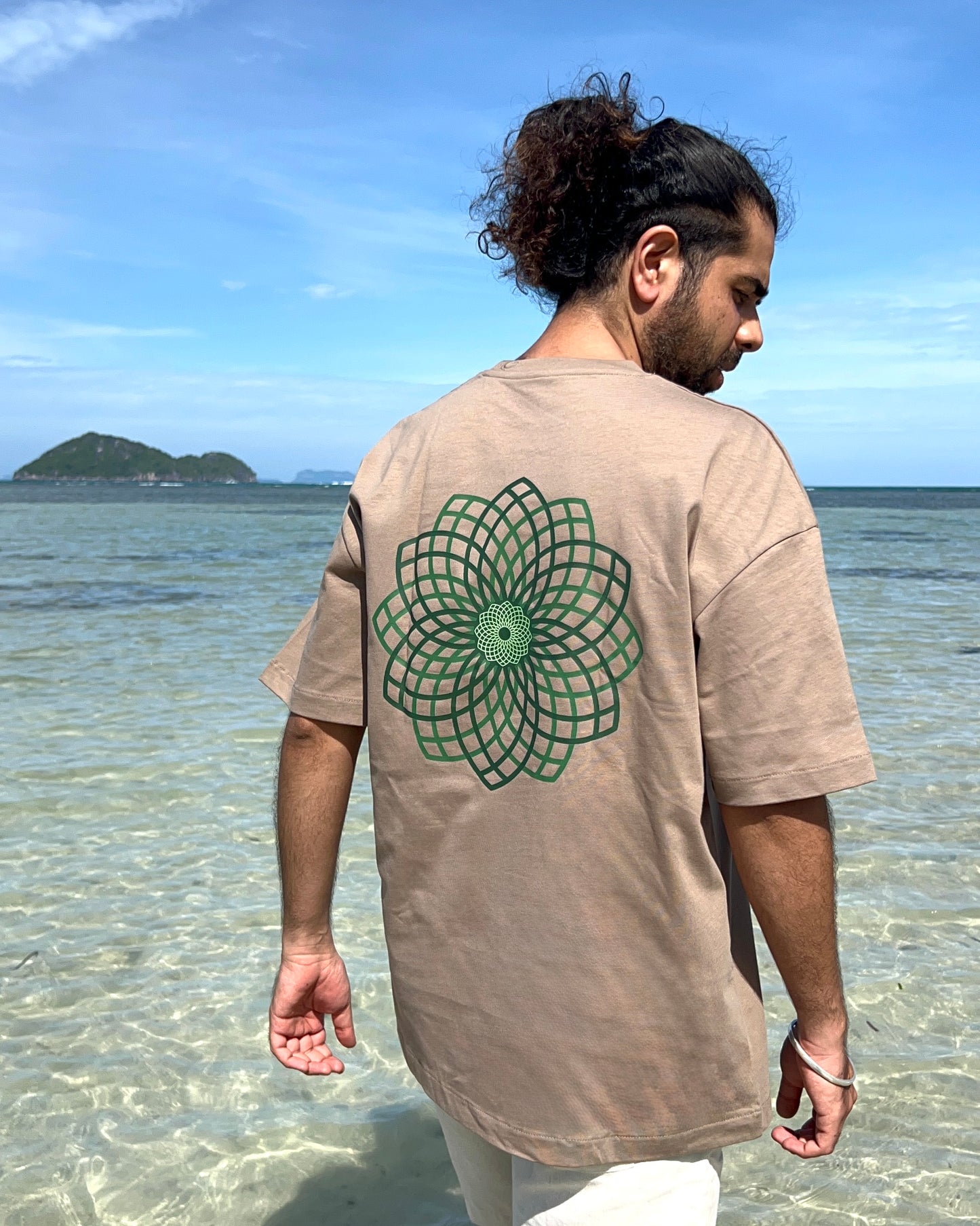 Man wearing a beige t-shirt with a green geometric design on the beach