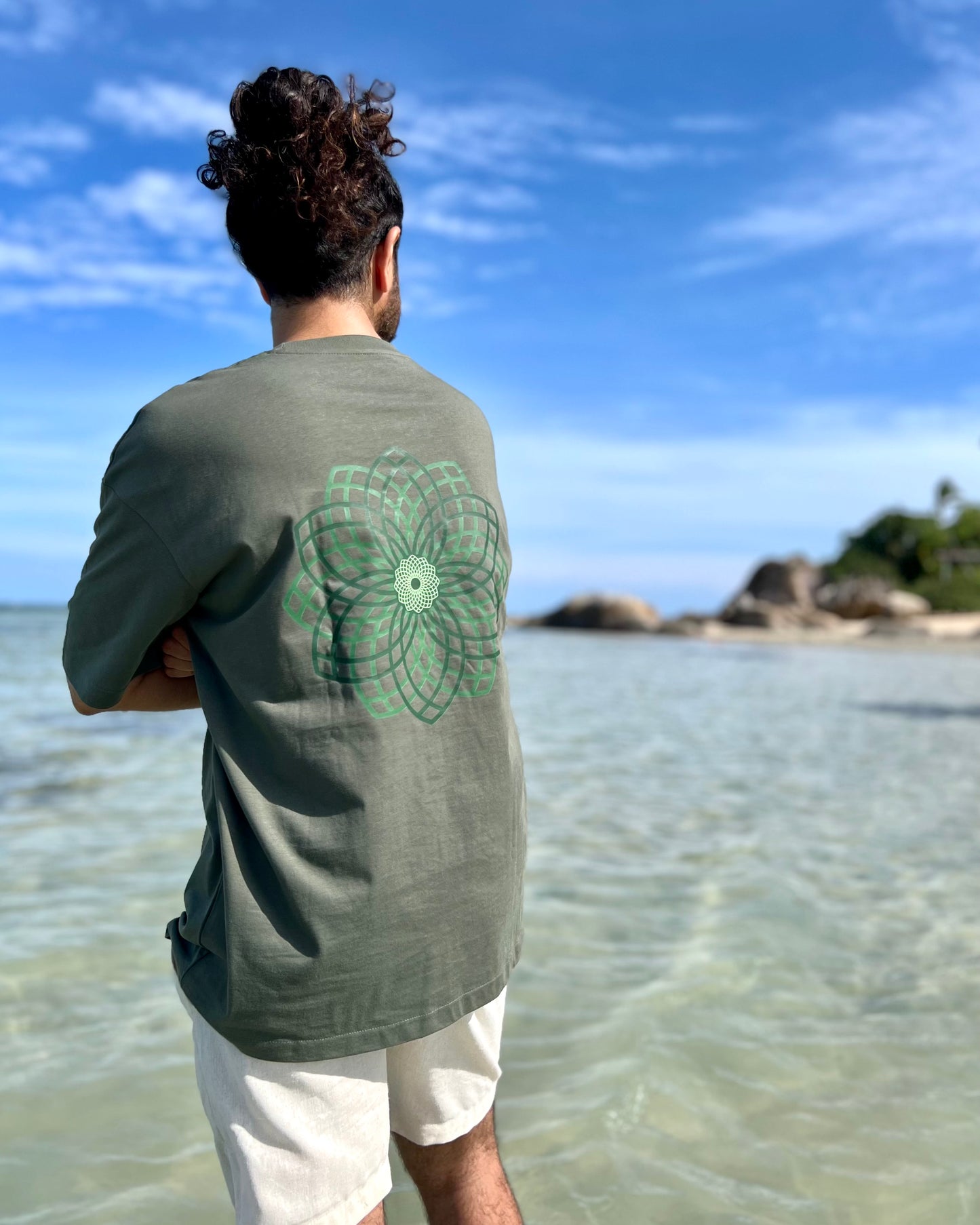 Person wearing a green t-shirt with a floral design standing on a beach.