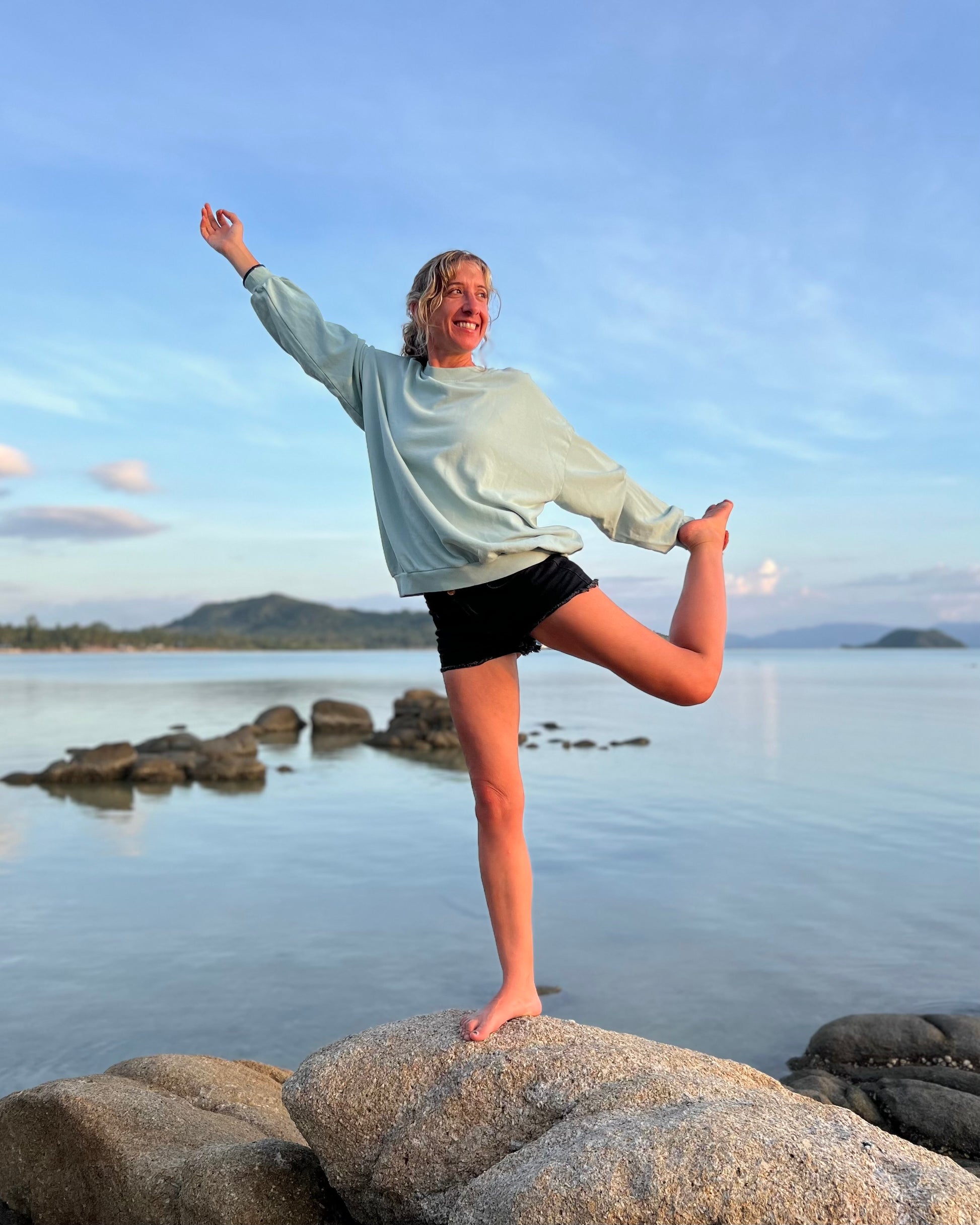 Person practicing yoga on rocks by a body of water with mountains in the background
