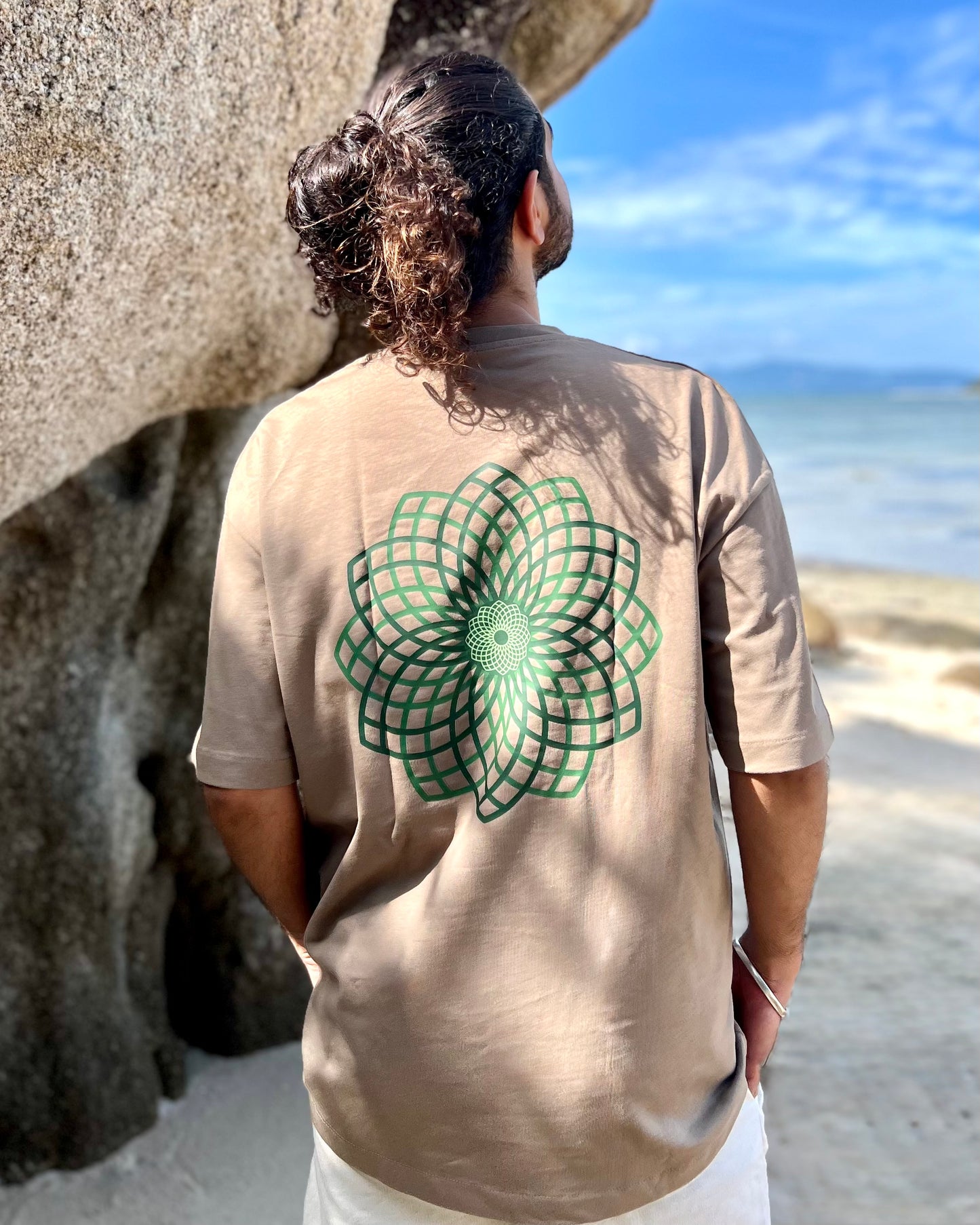 Person wearing a beige t-shirt with a green geometric design on the beach