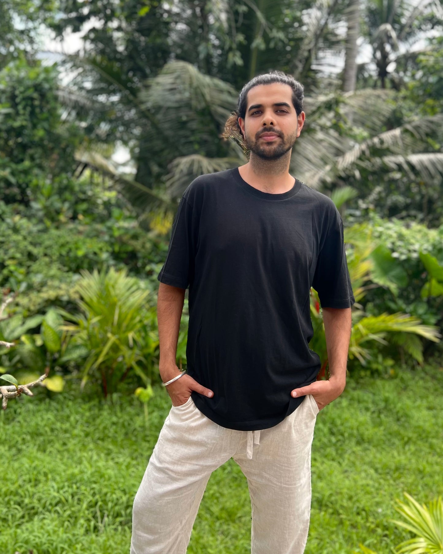 Man wearing a black t-shirt and white pants standing in a lush green outdoor setting