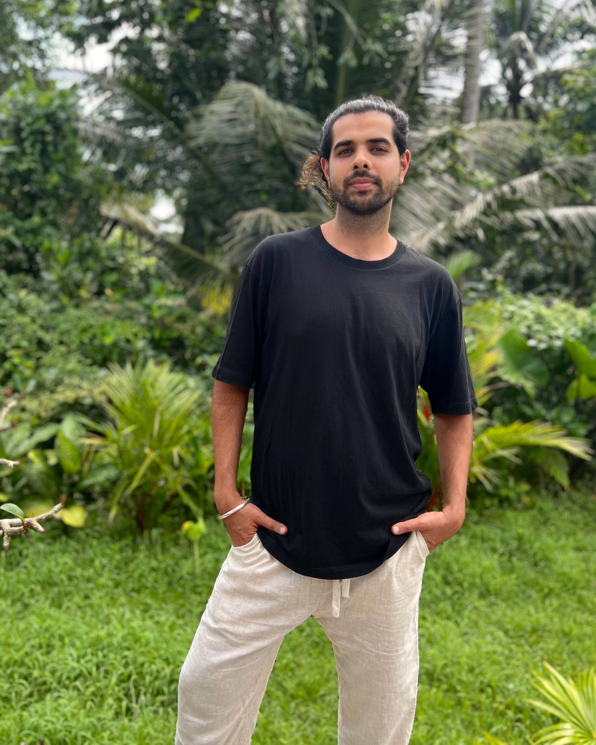 Man wearing a black t-shirt and white pants standing in a lush green outdoor setting