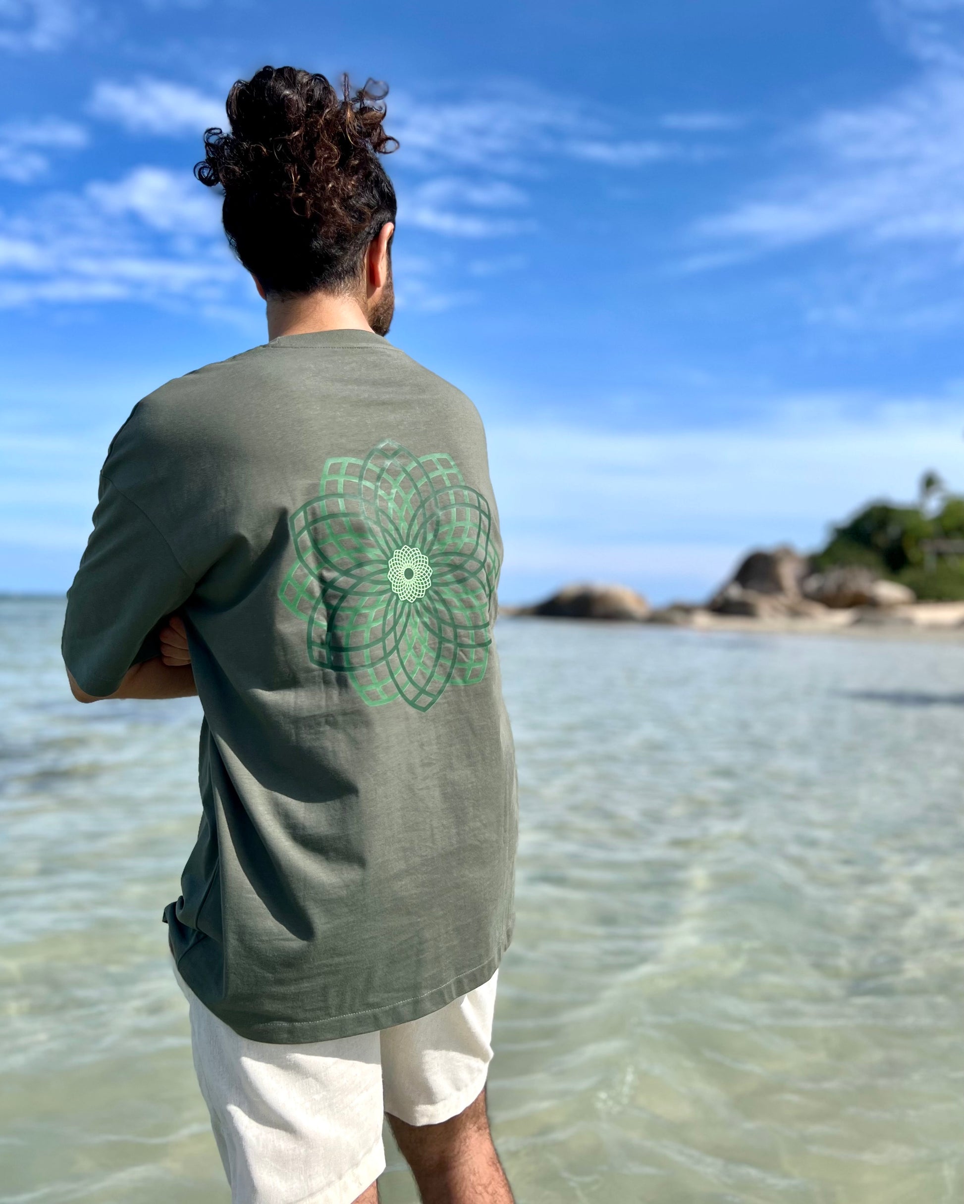 Person wearing a green t-shirt with a floral design standing on a beach.